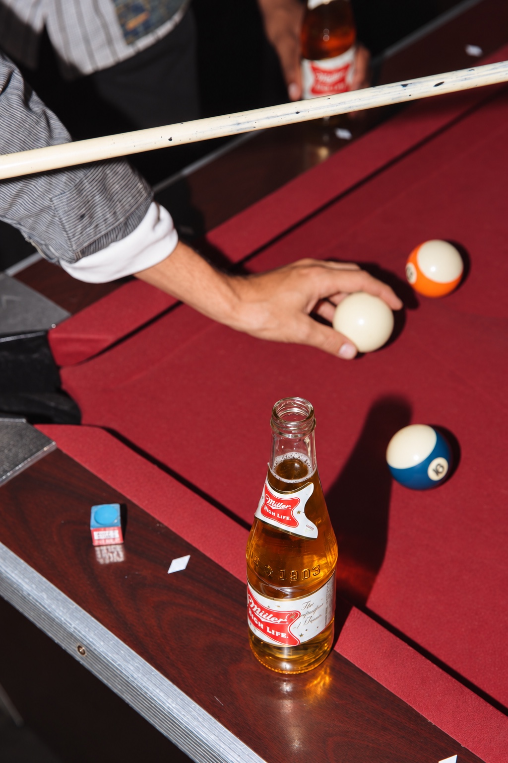 A beer bottle on the edge of a pool table during a game.