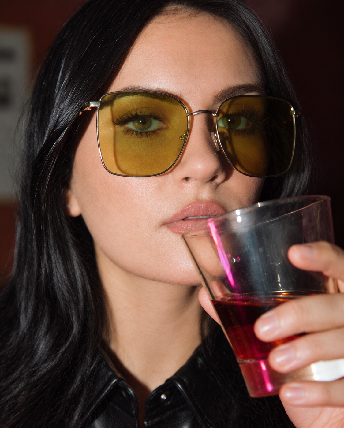 A woman wearing glasses and holding a whiskey glass.